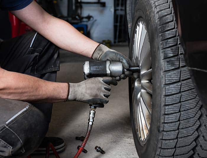 A wheel technician using an automatic screwdriver to tighten car wheels in a modern workshop