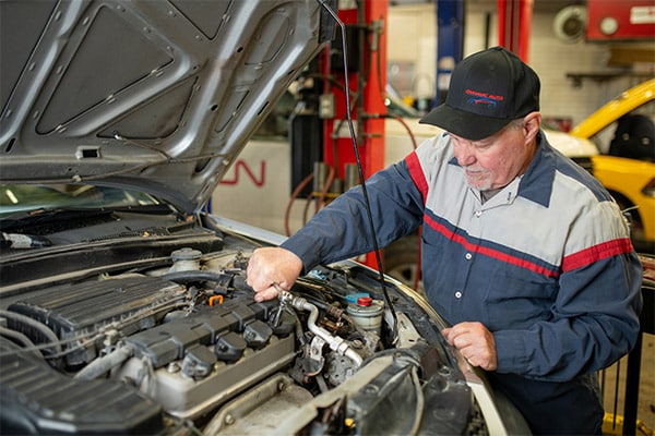 Mechanic working on a car engine inside an automotive service shop.