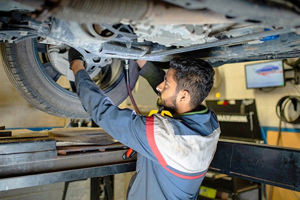 Technician performing maintenance under a vehicle on a lift in a repair facility.