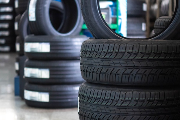 Stacked car tires in a store with various tire models on display. The image focuses on the treads and texture of the tires.